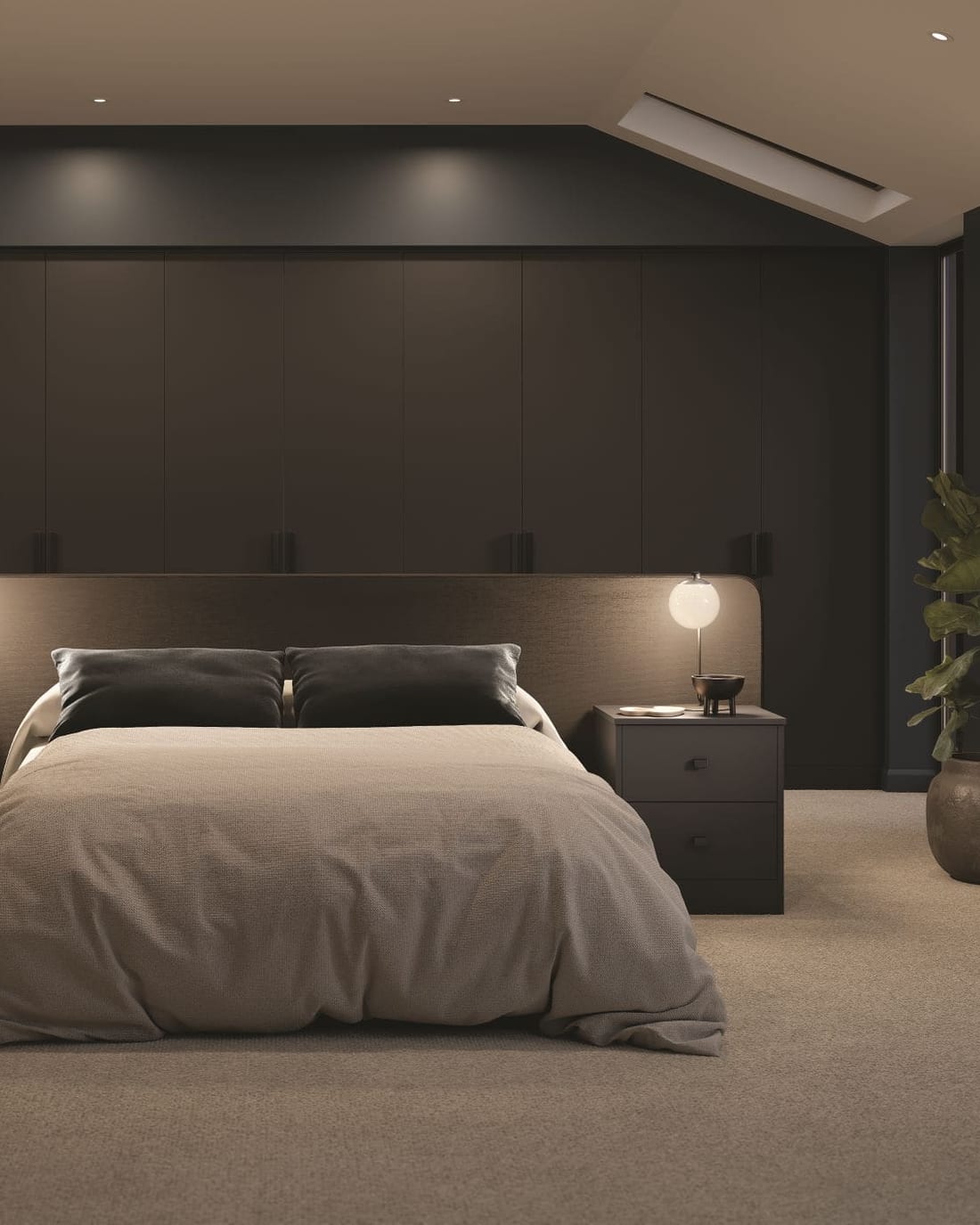 A wall of floor-to-ceiling fitted wardrobes in dark brown running the full width of a pitched-ceiling bedroom, with an integrated headboard and matching bedside drawer units.