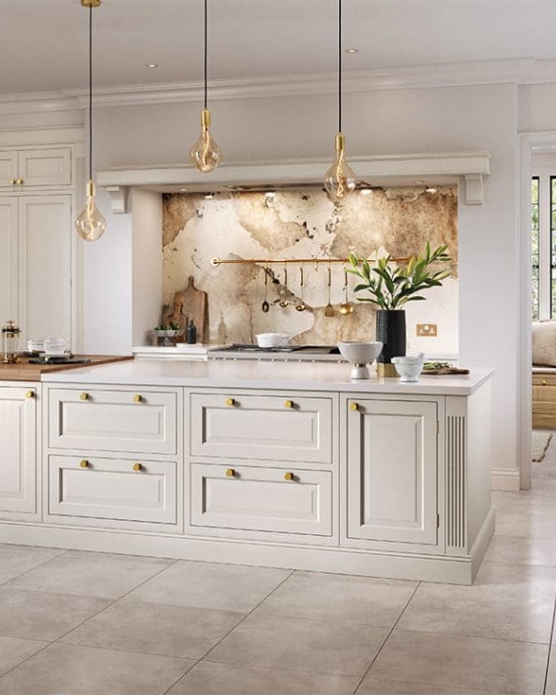 A cream in-frame kitchen island with two banks of inset drawers and brass knobs, an oak breakfast-bar return, and glass pendants hanging above.